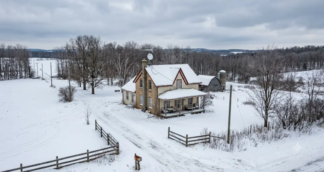 Rural Ontario farmhouse in winter with an internet antenna on the roof, snowy field and bare trees, illustrating limited rural connection options